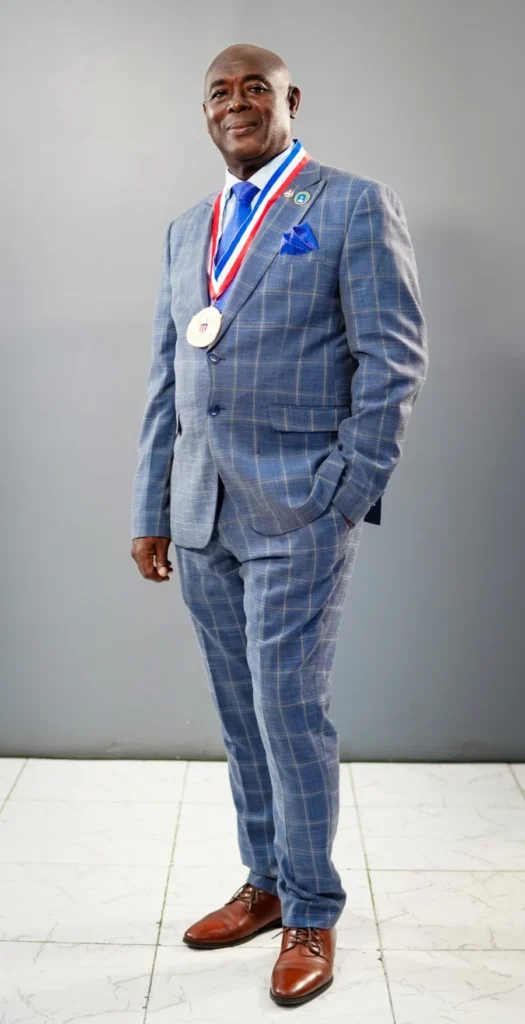 Full-length portrait of Bishop Donald Washington McFarlane, JP, in a blue checked suit with a ribbon and medal.