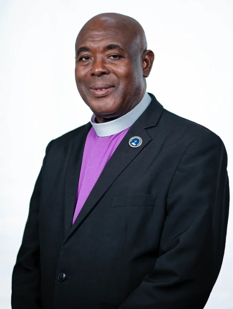 Portrait of Bishop Donald W. McFarlane, JP, Senior Pastor of New Foundation Christian Ministries, wearing a purple clergy shirt and black jacket.