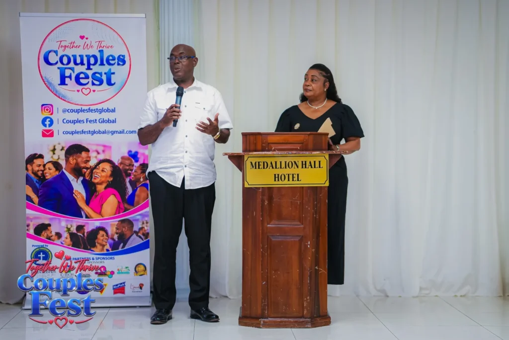 A man speaking into a microphone and a woman standing at a podium beside the Couples Fest “Together We Thrive” banner.