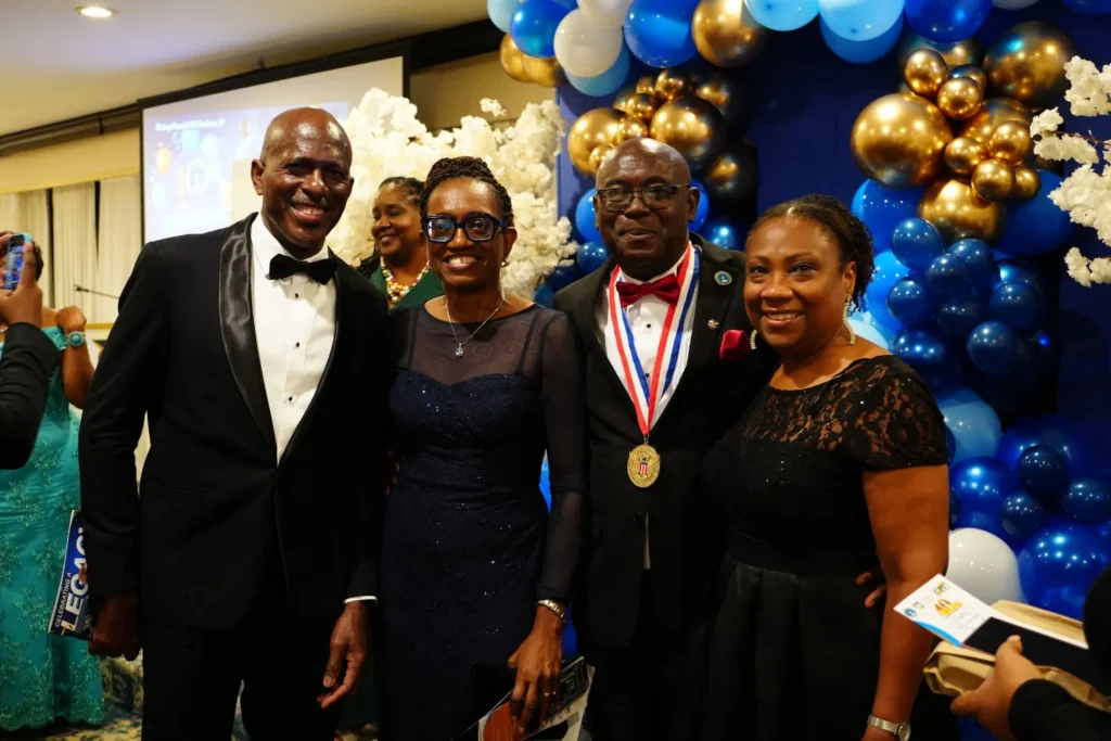 Bishop Donald McFarlane, wearing his medal, with guests in front of the blue and gold balloon arch at his 40th anniversary banquet.
