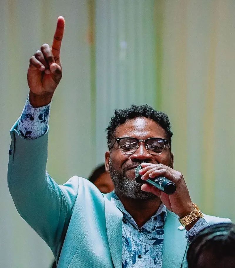A man in a mint blazer points upward in praise while singing at the NFCM Prayer Breakfast 2026.
