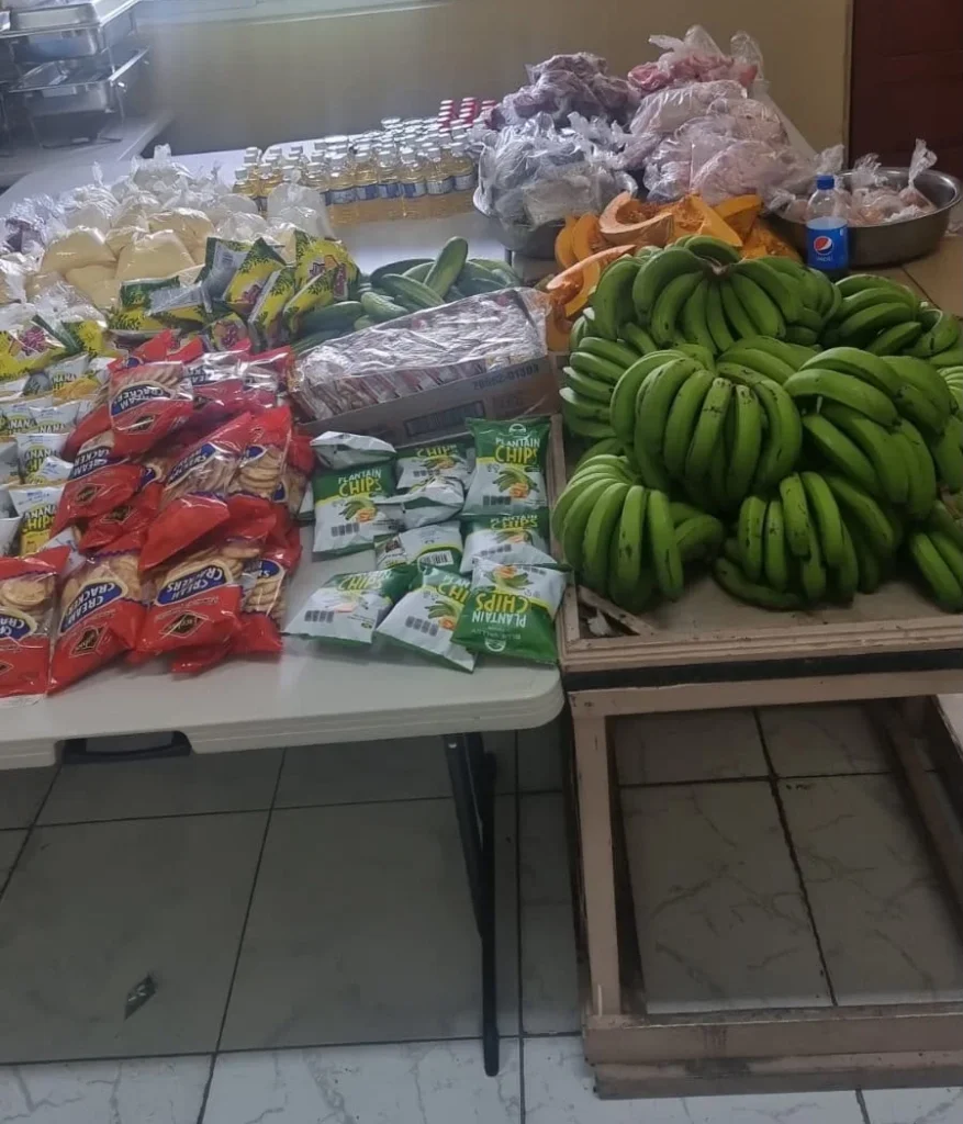 A table of green bananas, pumpkin, crackers, plantain chips and cooking oil prepared for families by the NFCM Pantry.